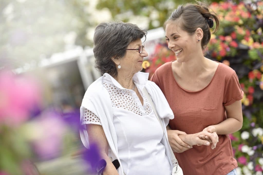 Une dame âgée souriante accompagnée par son auxiliaire de vie ARTEMIS au marché aux fleurs
